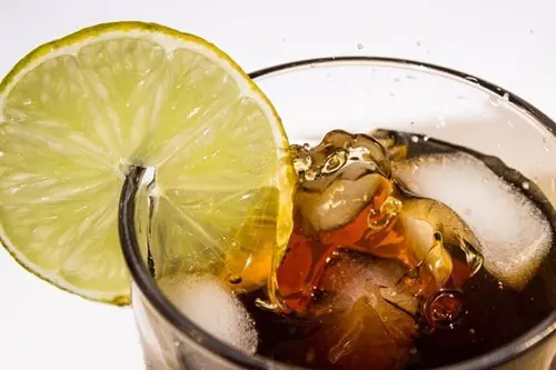 A glass of coke with a slice of lemon and ice